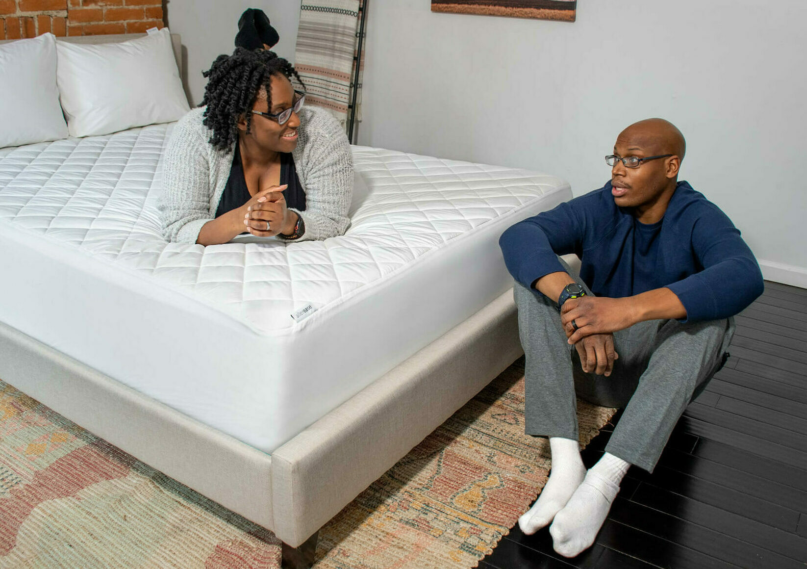 A woman on her bed talking to a man sitting on the floor.