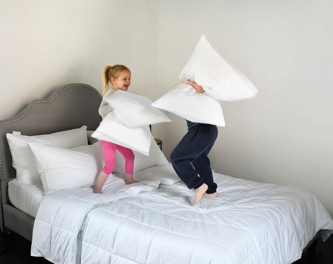 Two little kids having a pillow fight on the bed.
